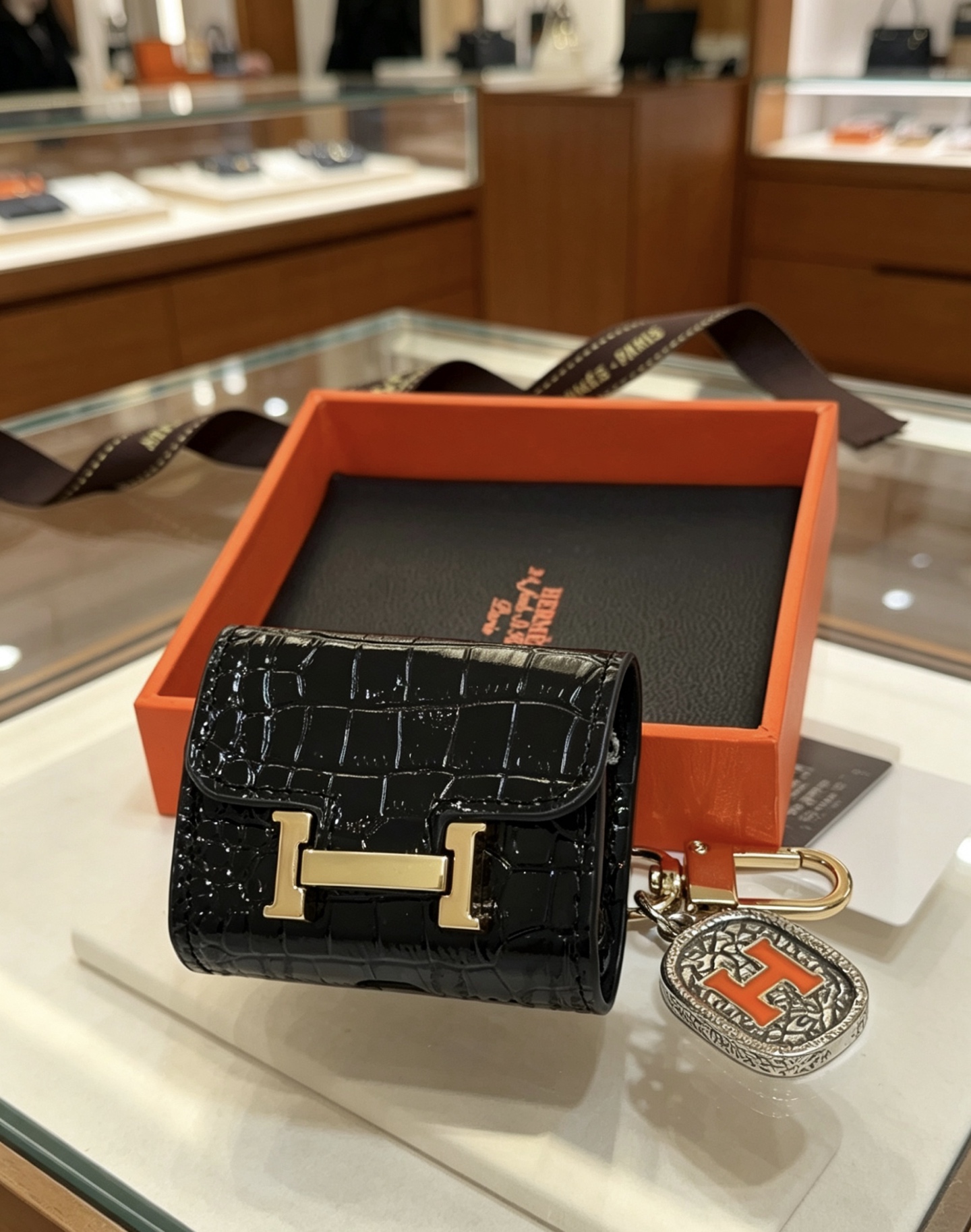 Hermes Constance Custodia per AirPods Borsa Ciondolo con ciondolo Pelle verniciata nera goffrata in coccodrillo Hardware in metallo color oro Ciondolo in metallo color argento con dettaglio H in smalto arancione Taglia unica adatta al ciondolo AirPods standard, lunghezza totale circa 8 cm