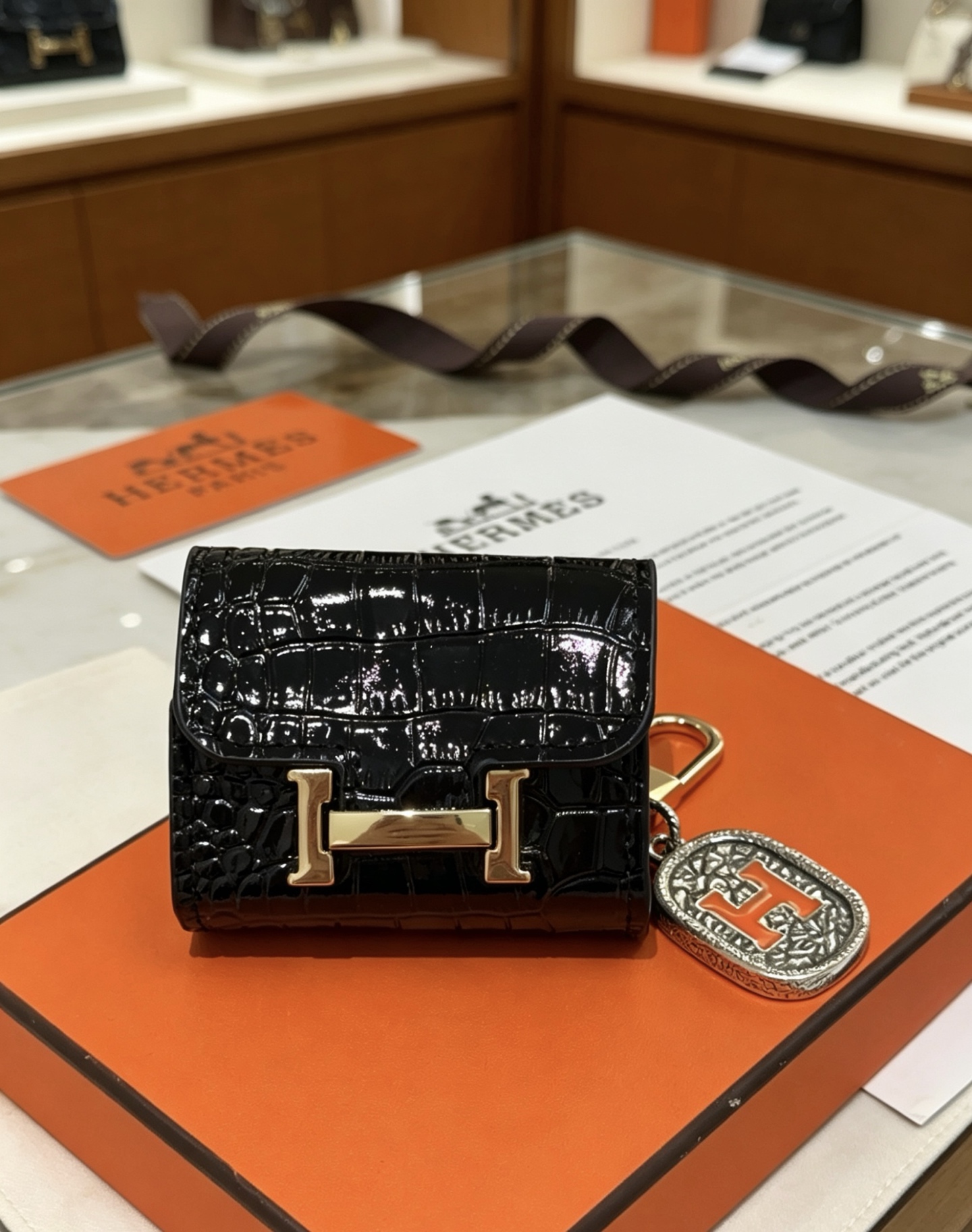 Hermes Constance Custodia per AirPods Borsa Ciondolo con ciondolo Pelle verniciata nera goffrata in coccodrillo Hardware in metallo color oro Ciondolo in metallo color argento con dettaglio H in smalto arancione Taglia unica adatta al ciondolo AirPods standard, lunghezza totale circa 8 cm