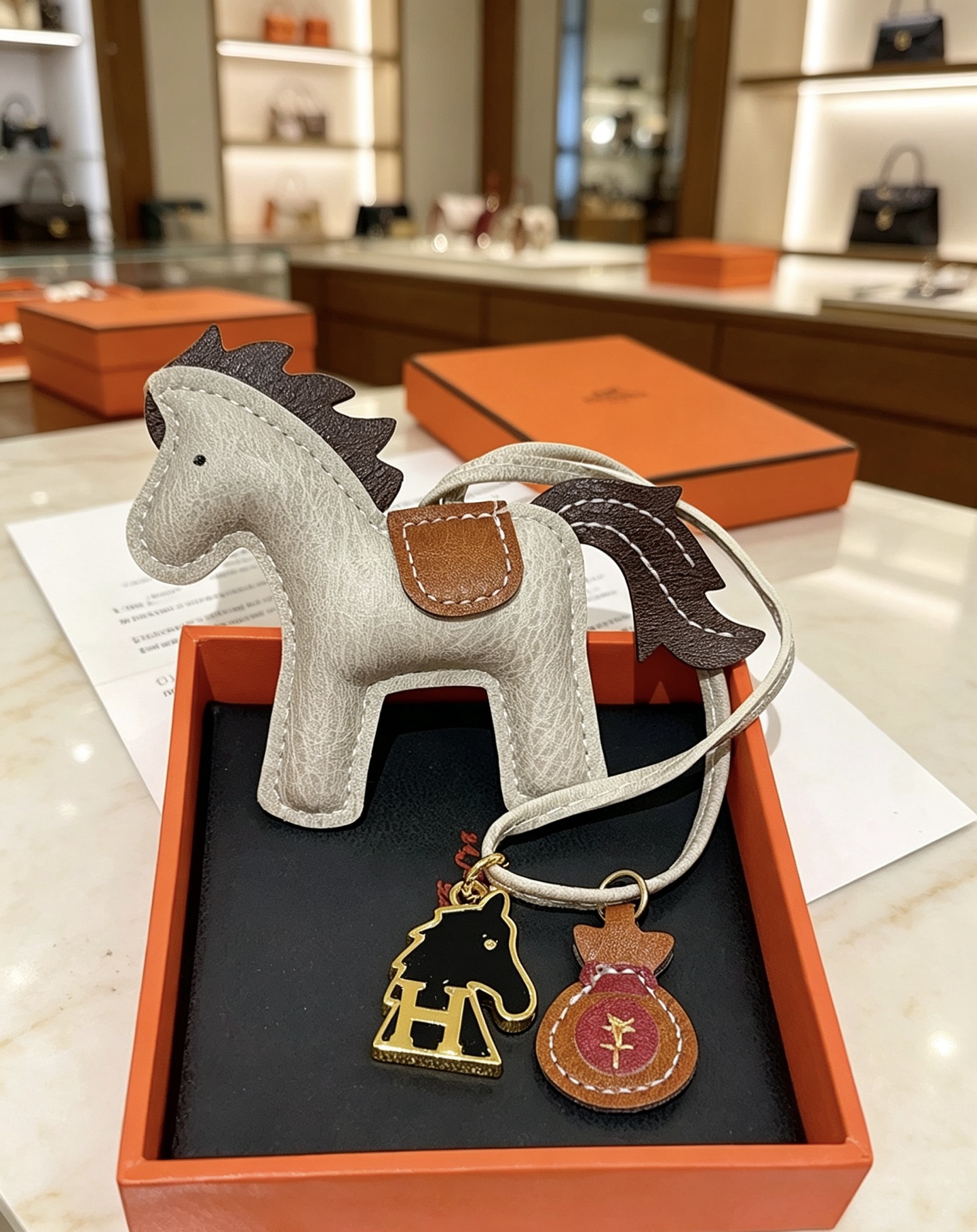 Ciondolo Hermes Rodeo Pegase Horse Bag Charm in pelle grigio chiaro con coda di criniera in pelle marrone scuro, sella in pelle marrone chiaro, hardware in metallo color oro, smalto nero, H cavallo, ciondolo per borsa di denaro in pelle bordeaux, ciondolo da 8 cm con cinturino in pelle da 12 cm.