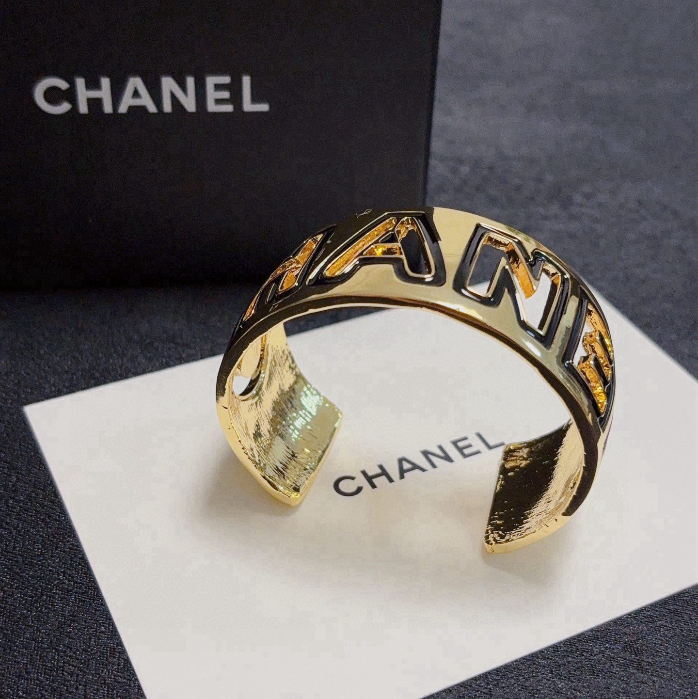 Chanel CHANEL Logo Cutout Wide Cuff bracelet Gold-tone metal with white enamel outlined cutout CHANEL lettering One Size adjustable open cuff fits 15-18cm wrist circumference