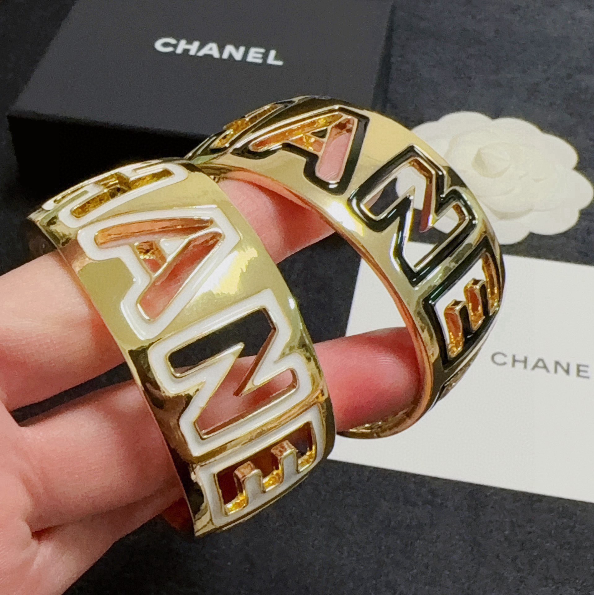 Chanel CHANEL Logo Cutout Wide Cuff bracelet Gold-tone metal with white enamel outlined cutout CHANEL lettering One Size adjustable open cuff fits 15-18cm wrist circumference