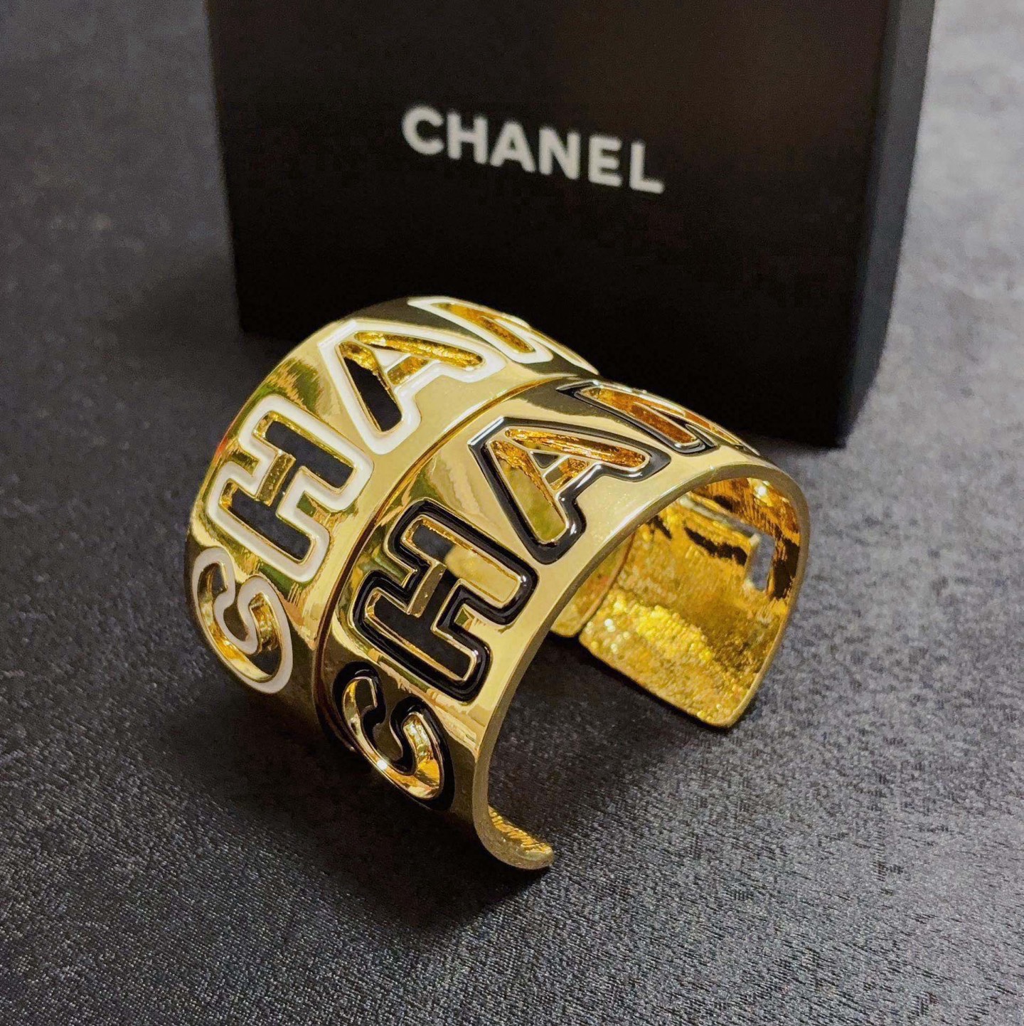 Chanel CHANEL Logo Cutout Wide Cuff bracelet Gold-tone metal with white enamel outlined cutout CHANEL lettering One Size adjustable open cuff fits 15-18cm wrist circumference